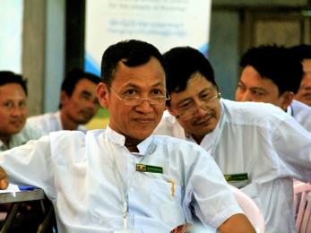 A person sits attentively while surrounded by other people in myanmar. 