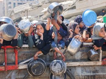 Palestinians holding empty pots and pans await a food delivery