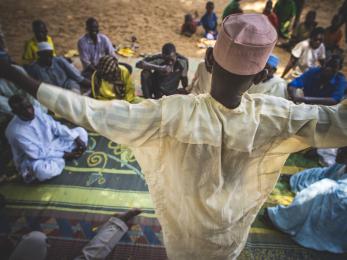 Nigerian man stands above community members he's speaking with.
