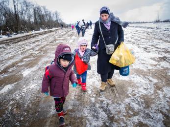 Woman with two young children walking with bags across snow-covered landscape