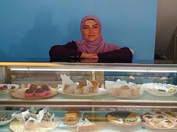 A business owner leaning on a display case of baked goods.