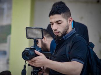 A photographer adjusts the settings on a camera mounted to a tripod.