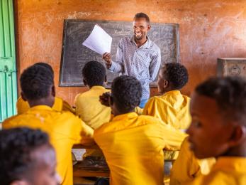 An adult teacher smiling at a classroom of young students.