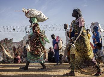 Sudanese refugee and South Sudanese returnee families walking along a barb wire fence.
