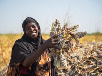 Sudanese woman poses with her sorghum harvest in celebration of a successful growing season.